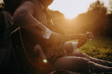 Çimenlerde oturan bir adam gitar çalıyor.