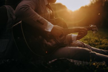 Çimenlerde oturan bir adam gitar çalıyor.