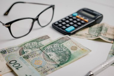 Hesap makinesi, gözlük, para ve kalem masada..