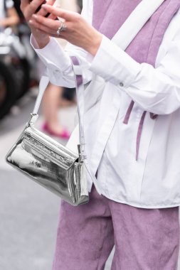 Milan, Italy - September, 21, 2022: Street style outfit, woman wears pale purple wool sleeveless, cropped gilet, matching pale purple wool large pants, silver shiny varnished leather handbag clipart