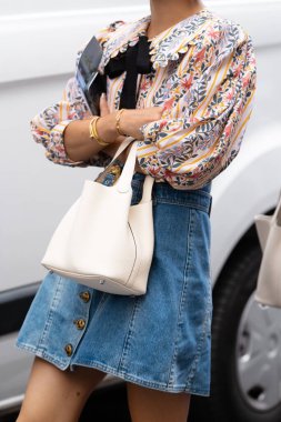 Milan, İtalya - 21 Eylül 2022: Sokak tarzı kıyafet detayları, kadın çiçekli desenli bluz, kısa kot mini etek ve bej deri çanta giyiyor. Çantayı tutan kadın. Günlük konsepti