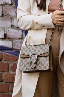 Milan, Italy - September, 21, 2022: woman wearing beige and brown GG monogram print pattern crossbody bag from Gucci, Dionysus GG Supreme mini bag, street style outfit details. clipart