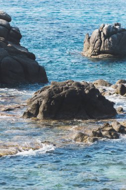 Vahşi kayalık sahil kıyısı ve deniz, dalgalar deniz kıyısındaki kayalara vurur, sakin deniz. Kıyıdaki kayalara dalgalar kırıyor beyaz deniz köpüğü ve küçük kabarcıklar yaratıyor.