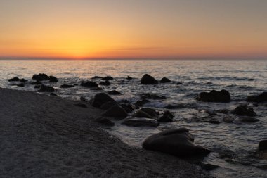 Beautiful view of orange sunset with rocks in Calabria, Mediterranean Sea, Italy. Tropical colorful sunrise landscape. Seascape
