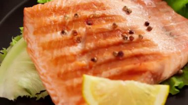 Izgarada yavaş yavaş dönen lezzetli somon balığı. Biberiyeli ızgara balık, salata ve limon. Yemek hazırlama, sağlıklı diyet konsepti, yakın çekim görüntüleri.