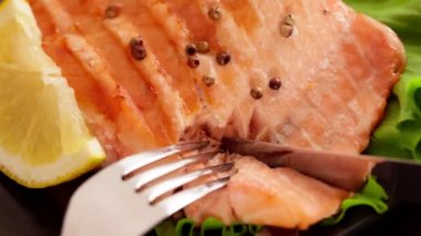 Izgarada pişmiş, bıçakla kesilmiş lezzetli somon balığı. Biberiyeli ızgara balık, salata ve limon. Yemek hazırlama, sağlıklı diyet konsepti, yakın çekim görüntüleri.