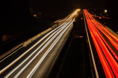 Yoldaki gece trafik ışıklarının soyut görüntüsü. Eğri asfalt yolda gece araba ışığı izleri var. Köprüdeki veya İHA 'daki arabaların hareketlerini gösteren uzun pozlama