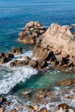 Kayalık sahillerde dalgalar, deniz kıyıları büyük kayaların üzerinde dalgalar eziliyor, yaz güneşli bir gün.