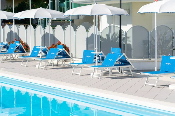 Grab bars ladder in the blue swimming pool, empty chaise longue, private swimming pool near hotel