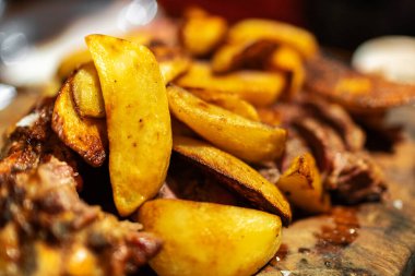 Ahşap masada biftek ve sos ile fırında patates dilimleri, restoranda yemek.