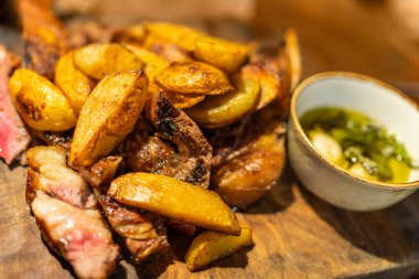 Ahşap masada biftek ve sos ile fırında patates dilimleri, restoranda yemek.