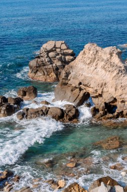 Kayalık sahillerde dalgalar, deniz kıyıları büyük kayaların üzerinde dalgalar eziliyor, yaz güneşli bir gün.