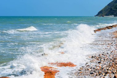 Rocky sahil şeridi. Rimini, İtalya 'da deniz dalgası arka planında kayalık kıyıda dalgalı turkuaz su kırılıyor. Deniz ufkuyla deniz manzarası ve açık mavi gökyüzü.