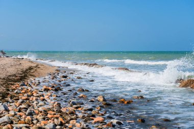 Rocky sahil şeridi. Rimini, İtalya 'da deniz dalgası arka planında kayalık kıyıda dalgalı turkuaz su kırılıyor. Deniz ufkuyla deniz manzarası ve açık mavi gökyüzü.