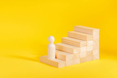 İşadamı merdivenleri çıkıyor. İş büyüme süreci, kariyer merdiveni. Hırs konsepti. Sarı arkaplanda tahta heykel