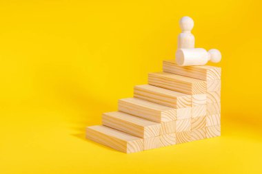 İşadamı merdivenleri çıkıyor. İş büyüme süreci, kariyer merdiveni. Hırs konsepti. Sarı arkaplanda tahta heykel