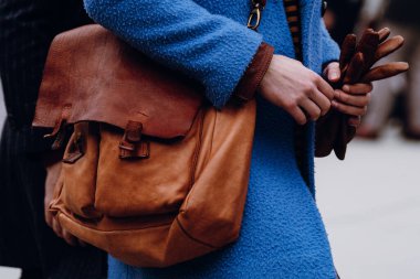 Floransa, İtalya - 12 Ocak 2022: Elinde kahverengi deri eldivenler ve pirinç donanımlı ve şık kış aksesuarları olan kırsal deri omuz çantası olan mavi ceketli kişiye yakın çekim