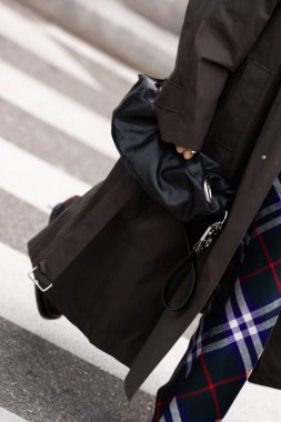 Milan, İtalya - 14 Ocak 2024: Koyu renk trençkot ve ekose pantolonlu modaya uygun bir şekilde şehir caddesinde yakalandı. Deri ve kumaş gibi detaylı dokulara odaklanmak, 