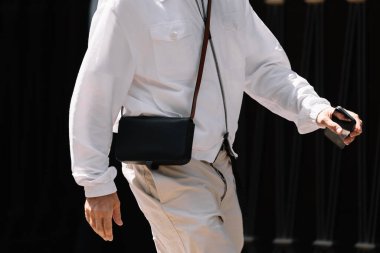 Milan, İtalya - 19 Haziran 2023: Kırmızımsı beyaz gömlek ve bej pantolonla tamamlanmış minimalist siyah çapraz vücut çantasının görüntüsü.