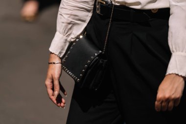 Milan, İtalya - 16 Haziran 2023: Beyaz bluzlu bir kadın tarafından tutulan, metal çivili siyah el çantasının moda fotoğrafları. Modern gardırop için mükemmel bir aksesuar.