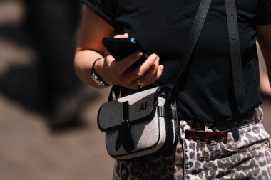 Milan, İtalya - 16 Haziran, 2023: Gelişigüzel kentsel ortamlarda şık monogramlı çapraz vücut çantalarına yakın çekim. Akıllı telefon tutan kişi, kıyafet ayrıntıları.