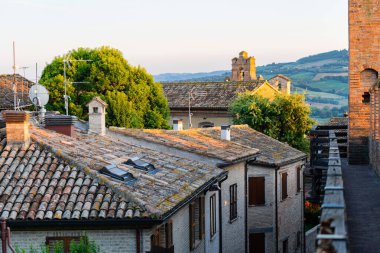 Gradara, İtalya - 25 Ağustos 2022: Gün batımında yemyeşil ve uzak tepeleri olan gradara köyünün çatıları