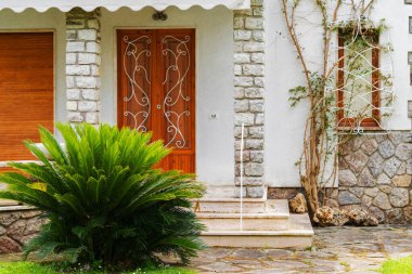 Tahta kapıları, taş sütunları ve yemyeşil bitkileri olan büyüleyici bir evin ön girişi.