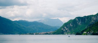 Göl manzarası bulutlu gökyüzünün altında dağlarla ve köyle çevrili.