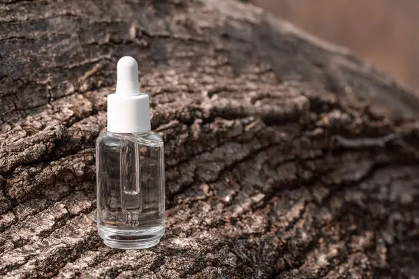 stock image clear serum bottle with white dropper cap sits on weathered bark, showcasing natural beauty and skincare synergy.