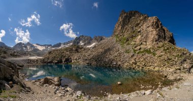 Durgun dağ gölü kristal berrak suyla karlı tepeleri ve yüksek irtifada kayalık uçurumları yansıtıyor, el değmemiş doğayı ve engebeli güzelliği sergiliyor.