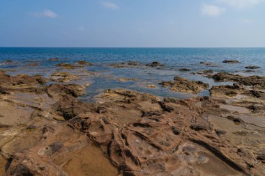 Sakin, mavi denizin ufka kadar uzandığı kayalık bir kıyı şeridinin sakin bir görüntüsü. Engebeli kayalar, dingin okyanusla çok güzel tezat oluşturuyor.