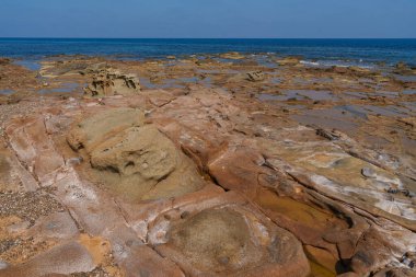 Kayalık bir kıyı şeridinde gelgit havuzları olan aşınmış kıyı kayaları, açık bir gökyüzünün altında mavi okyanus ufka kadar uzanıyor.