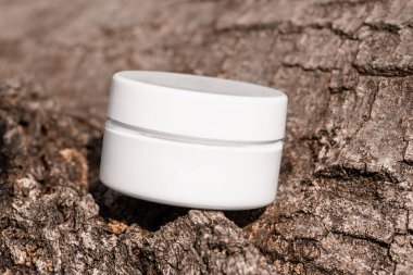 Engebeli ağaç kabuğuna yerleştirilmiş beyaz kozmetik cilt kremi kavanozu, cilt bakımı sunumu, serum losyonu şablonu, boş şişe ön görünüş modeli, organik yüz maskesi, eko konsepti.