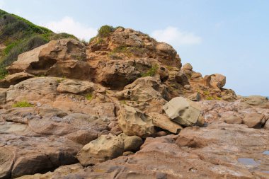 A rugged cliffside showcasing eroded rocks with minimal vegetation under a bright sky. A natural landscape highlighting the effects of weathering on coastal geology clipart