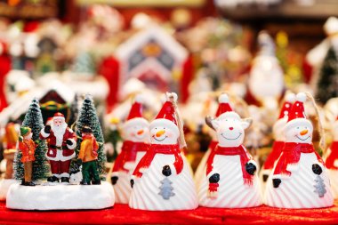 Kırmızı ve beyaz giyinmiş seramik kardan adam ve Noel Baba heykelcikleri yumuşak ışıklandırma ve renkli dekorasyonlarla bayram sahnesinde sergileniyorlar.
