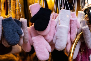 Pembe, siyah, gri ve beyaz tonlarında yumuşak, tüylü kış eldivenleri koleksiyonu, arka planda altın ışıkla sıcak, rahat bir ortamda sergileniyor.