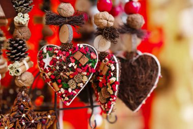 Kurutulmuş meyve, yıldız anason, tarçın ve dal gibi doğal elementlerle süslenmiş el yapımı kalp şekilli süsler, canlı kırmızı aksanlarla şenlikli bir şekilde sergileniyor.