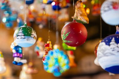 Parlak renkli, elle boyanmış Noel süsleri iplerden sarkıyor, çeşitli festival sahneleri ve karakterleri sergiliyor, neşeli bir tatil atmosferi yaratıyor.