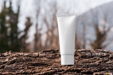 Engebeli ağaç kabuğu yüzeyinde beyaz kozmetik krem tüpü. Creme modelleme, podyumda marka ambalajlama, bakuchiol ile cilt ürünü, güneş kremi modelleme