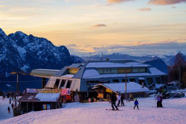 Piani di Bobbio, İtalya - 24.12.2022: Kayakçılar yüksek tepelerin ardında güneş batarken dağ restoranının yakınlarındaki karlı yamaçların tadını çıkarıyorlar. Sahne, kış kayak merkezinin güzelliğini ve etkinliğini yansıtıyor.