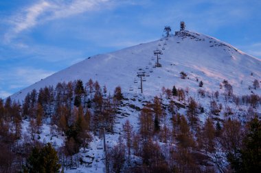 Piani di Bobbio, İtalya - 24.12.2022: Zirveye doğru yükselen başkanlık sırasına sahip karla kaplı dağ zirvesi. Açık mavi gökyüzü ve dağınık ağaçlar sakin bir kış manzarası yaratır.