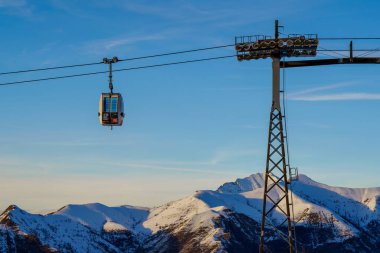 Piani di Bobbio, İtalya - 24.12.2022: Kablo araç çelik destek kulesinin yanından geçiyor. Kışın kayak merkezinde kayak yapan insanlar. Tatiller, kar giysileri kiralama, kayak, snowboard ve dağ manzarası konsepti