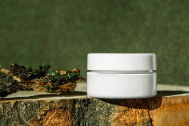 Kolajenle sıkılaştırılmış krem kavanozu yeşil toprak tonlu arka planda ahşap ekrana yerleştirilmiş. Creme modelleme, podyumda marka ambalajlama, cilt ürünleri, güneş kremi modelleme
