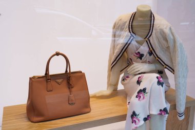 Milan, İtalya - 24.04.2024: Zarif mağaza vitrininde çiçekli elbise ve tasarımcı çantasıyla moda Prada sergisi.