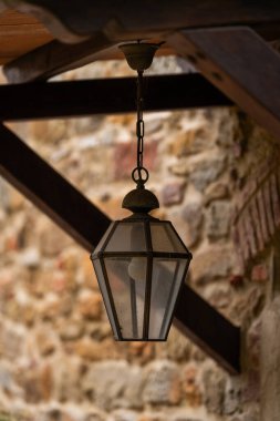 Köy taşından duvara dayanmış, ahşap kirişlerden sarkıtılmış klasik tarzda asılı fener. Sıcak tonlar ve dokulu malzemeler eski dünya atmosferini oluşturur..