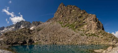 Kristal berrak su ile sakin dağ gölü dramatik uçurumları ve el değmemiş doğa ve engebeli araziyle çevrili el değmemiş dağlık bir çevrede kar kaplı tepeleri yansıtıyor.