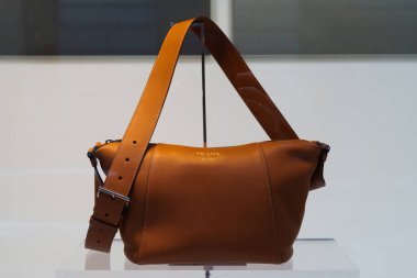 Milan, İtalya - 24.04.2024: Cam standda sergilenen şık kahverengi Prada deri çanta.