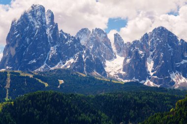 İtalya 'nın Dolomites kentindeki Funes Vadisi yakınlarında bulutlu bir gökyüzünün altında karla kaplı tepeleri ve yemyeşil ormanları olan görkemli dağ sıraları..