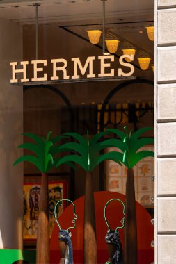 Milan, İtalya - 02.08.2023: Canlı Hermes vitrininde palmiye ağaçları ve lüks perakende tasarımı için neon figürler sergileniyor.