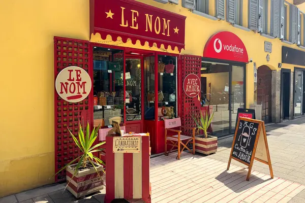 Milan, İtalya - Nisan 07, 2025: Le Nom butiğinin vitrininde kırmızı boyalı giriş, el yapımı çantalar, çizgili sandalyeler ve dekoratif unsurlar. Ön görünüm.